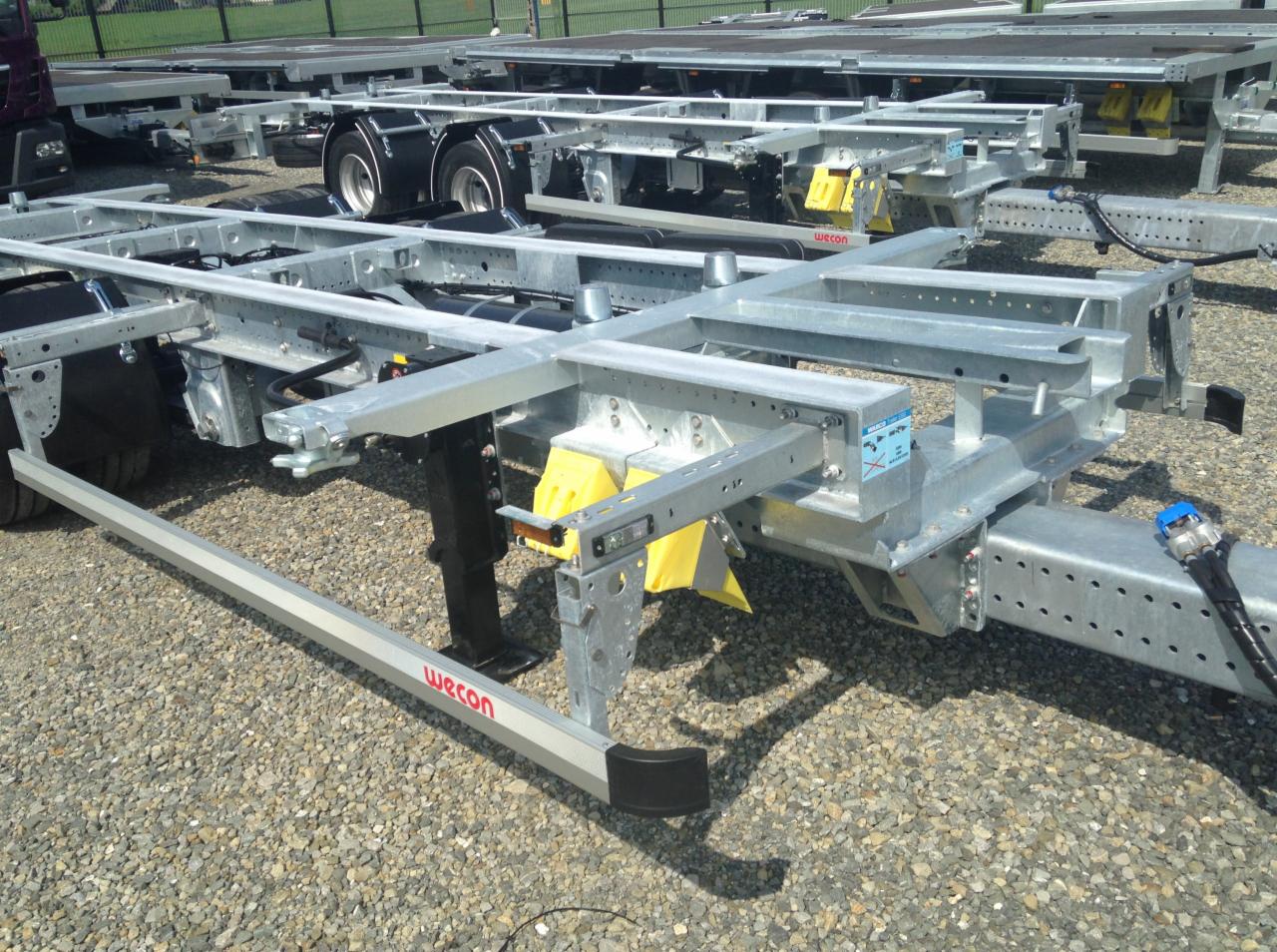 Stalowa rama naczepy z elementami zabezpieczającymi i widocznym logo 'Wecon' na listwie bocznej, na żwirowym placu.