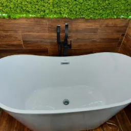 Wolnostojąca biała wanna z czarną armaturą na tle ściany z drewnopodobnych płytek i dekoracji z mchu, oświetlona delikatnym światłem.