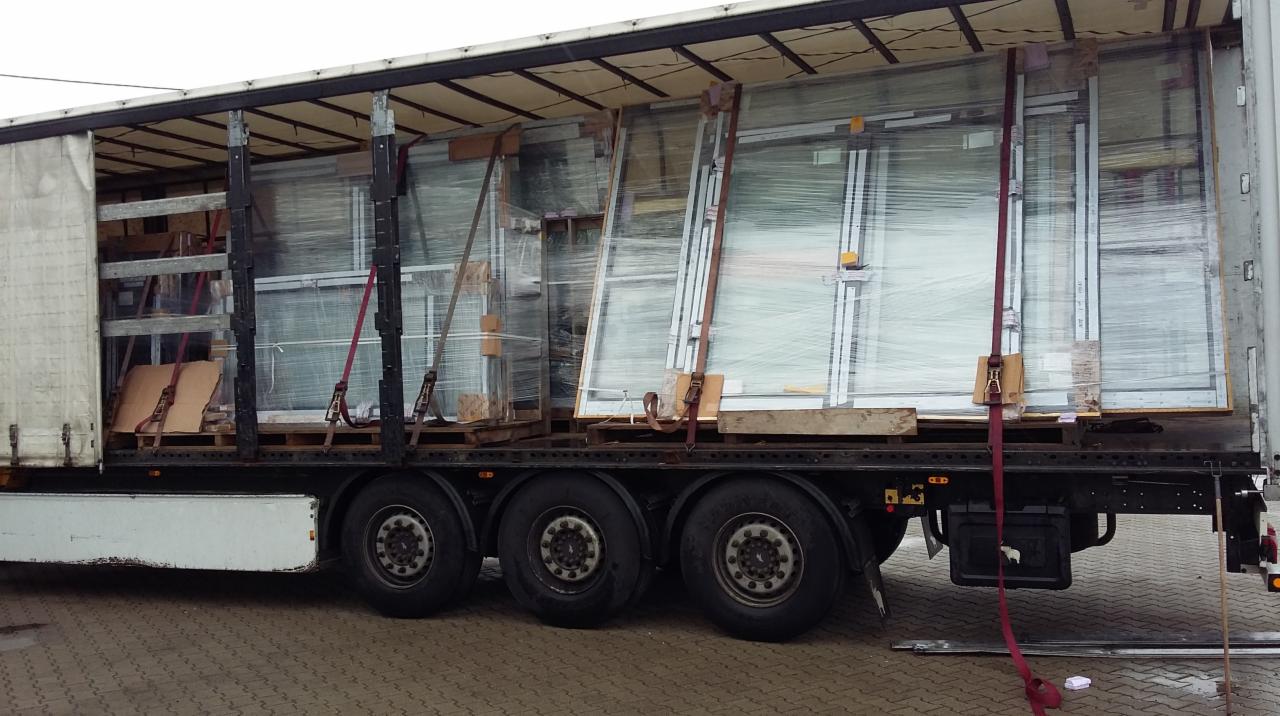 Transport okien w zabezpieczonej naczepie ciężarówki, okna owinięte folią stretch i przymocowane pasami transportowymi.