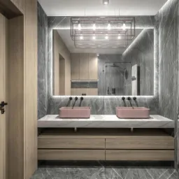 Nowoczesna łazienka z marmurowymi ścianami, podwójną umywalką w kolorze pudrowego różu, podświetlanym lustrem i drewnianymi szafkami pod umywalką.
