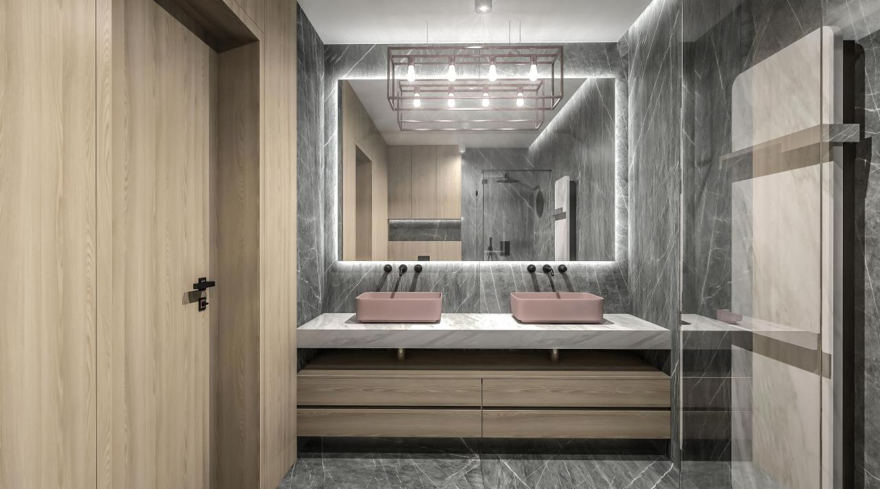 Nowoczesna łazienka z marmurowymi ścianami, podwójną umywalką w kolorze pudrowego różu, podświetlanym lustrem i drewnianymi szafkami pod umywalką.