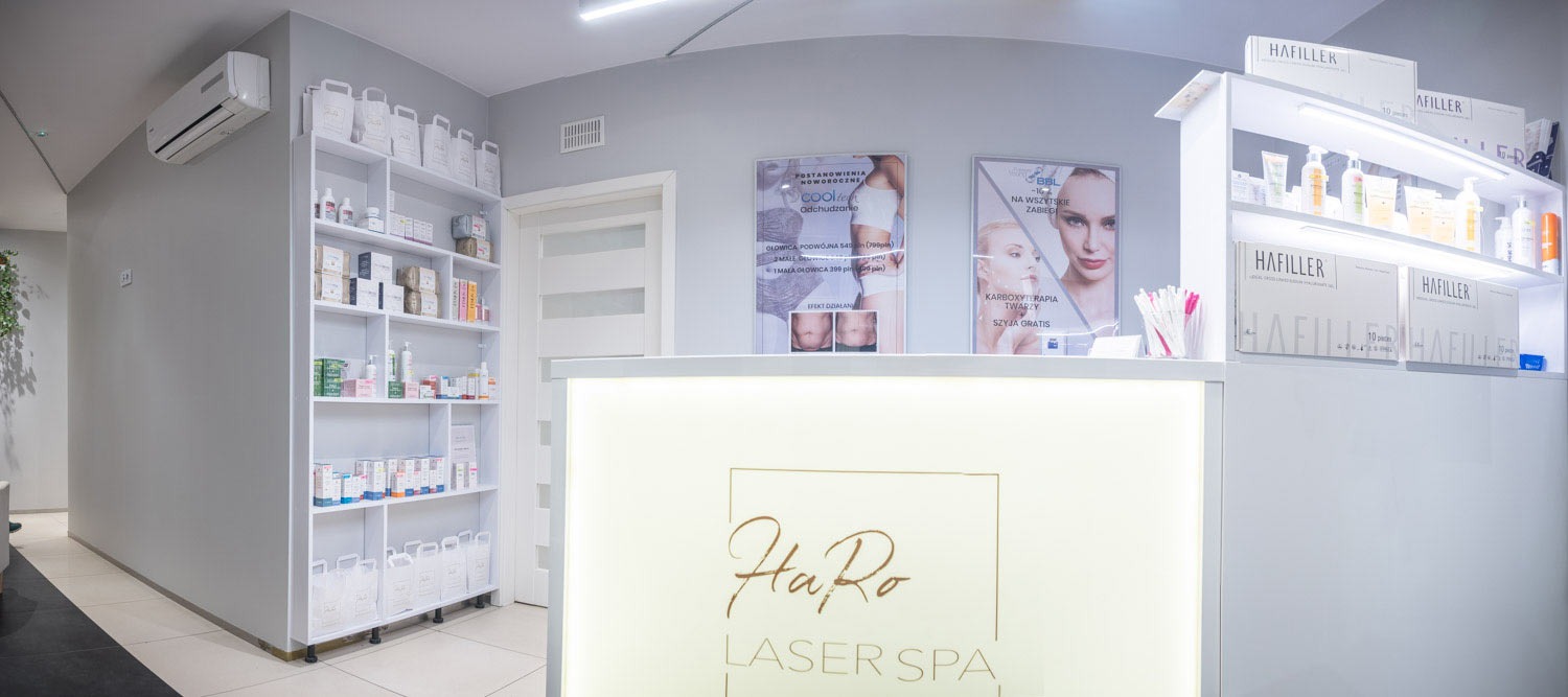 Wnętrze salonu medycyny estetycznej z recepcją podświetloną logo 'HaRo LASER SPA', półki z kosmetykami i produktami HaFiller, plakaty reklamowe zabiegów Cooltech i karboksyterapii.