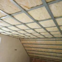 Ocieplenie poddasza wełną mineralną, widoczne metalowe profile konstrukcyjne, ściana z cegły w dolnej części pomieszczenia.