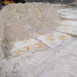 Świeżo wysypany materiał sypki w wyznaczonych kwaterach, widoczny fragment opony maszyny budowlanej w tle.