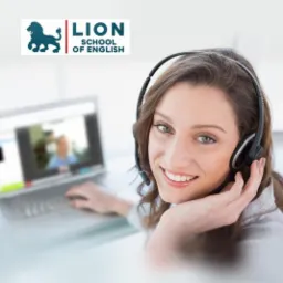 Uśmiechnięta kobieta z zestawem słuchawkowym prowadzi lekcję online, widoczna na ekranie laptopa.