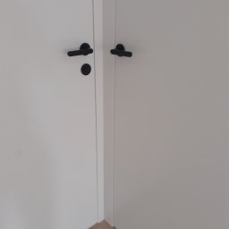 USŁUGI BUDOWLANE MONTERS ŁUKASZ SZYBAJŁO - Zamknięte białe drzwi wewnętrzne z czarnymi, minimalistycznymi klamkami i zamkiem.