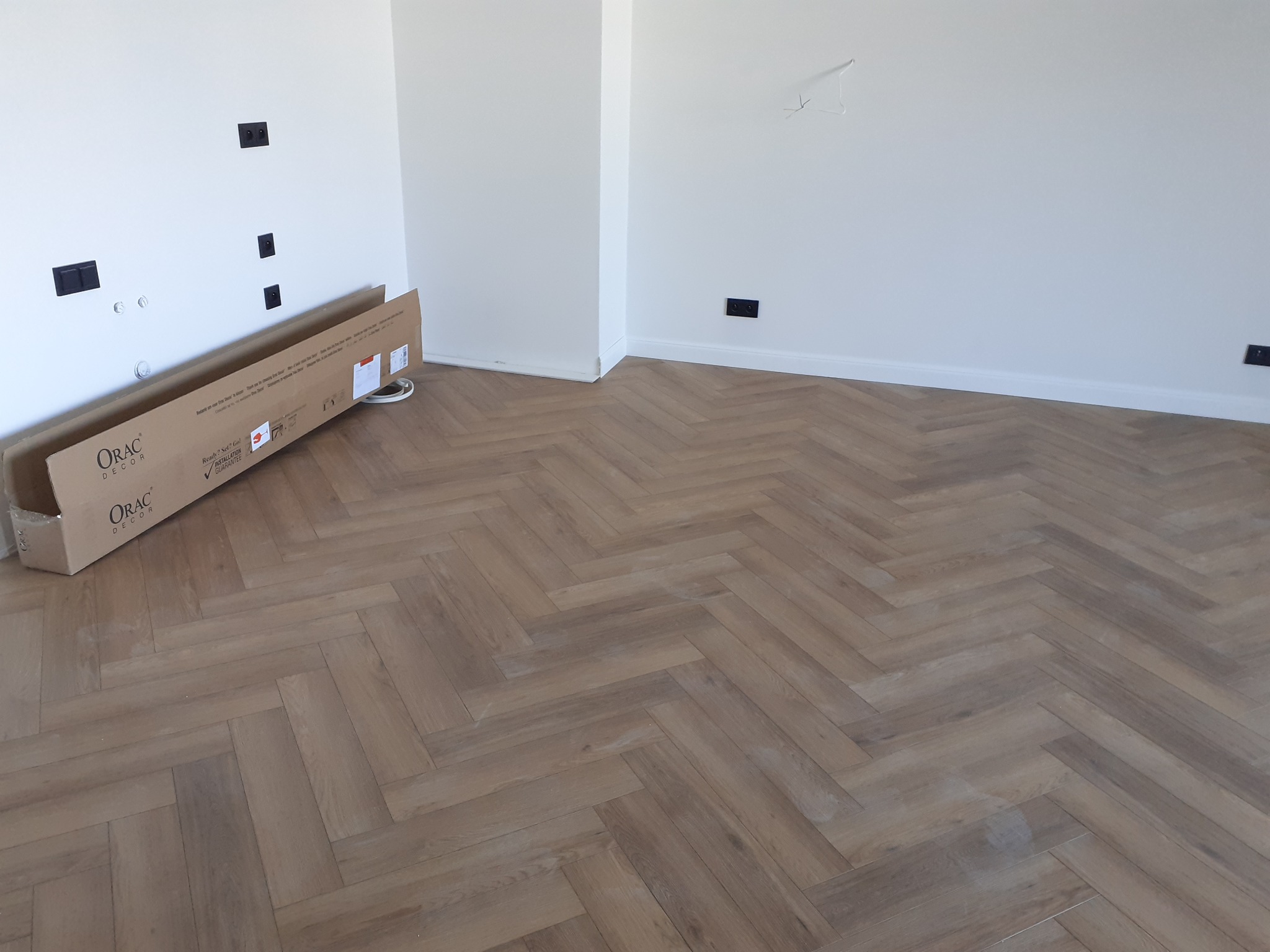 Ułożona podłoga z paneli w jodełkę francuską, karton paneli ORAC Decor przy ścianie z gniazdkami elektrycznymi.