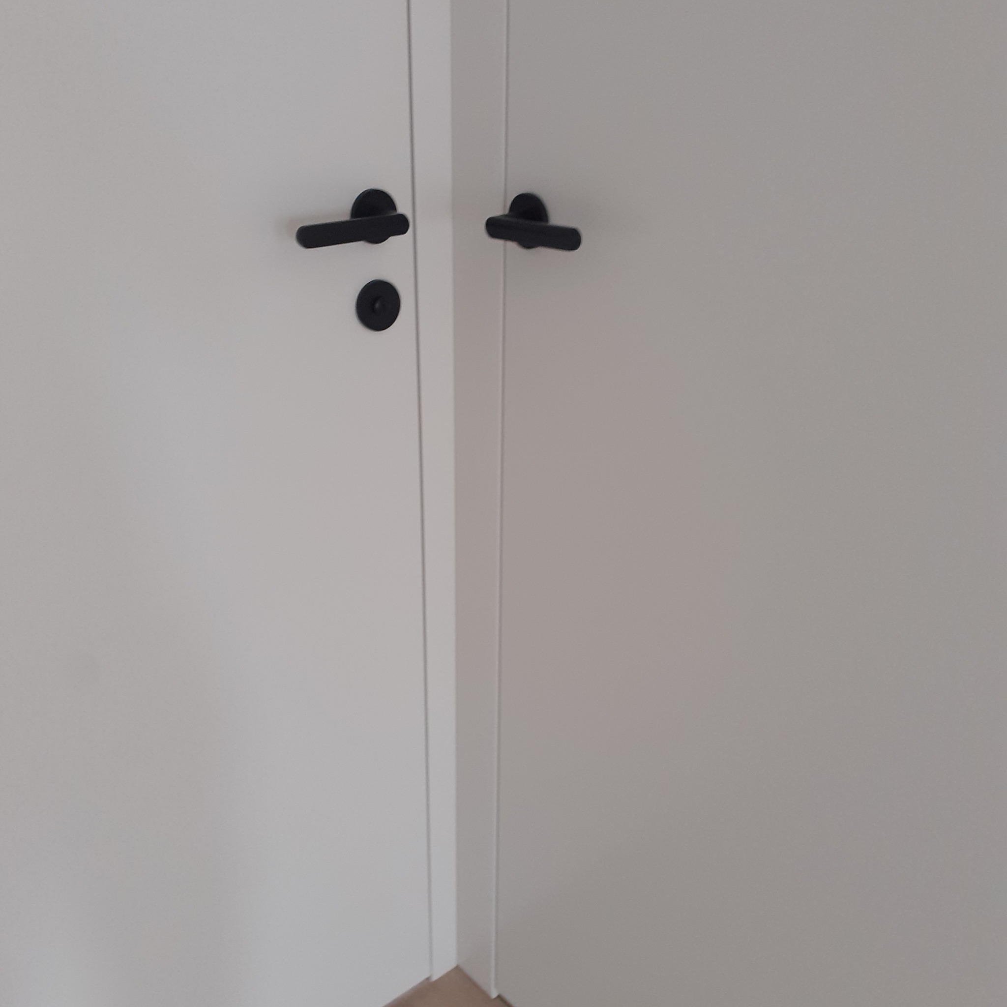 Zamknięte białe drzwi wewnętrzne z czarnymi, minimalistycznymi klamkami i zamkiem.