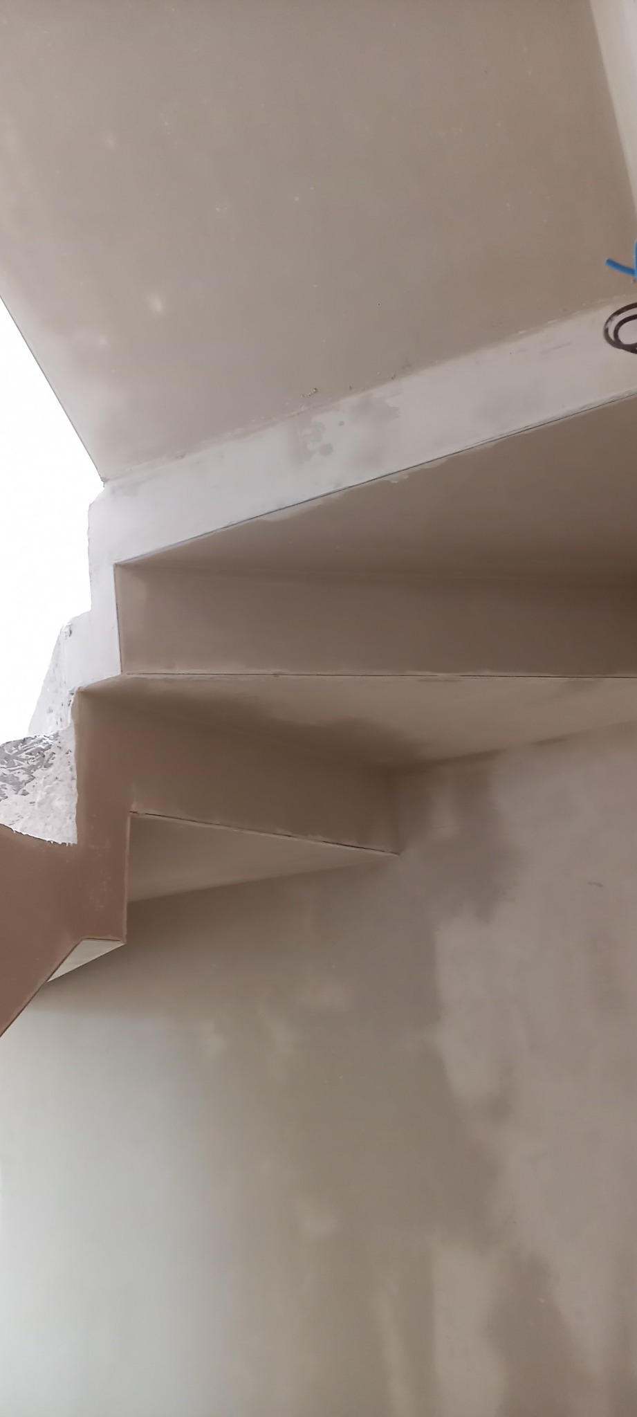 Wykończone, gładkie schody wewnętrzne po nałożeniu jasnej, jednolitej warstwy tynku maszynowego, widok z dołu.