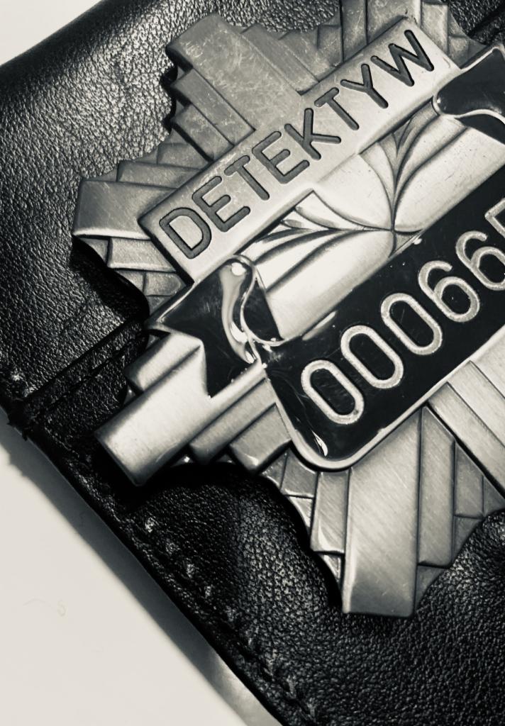Metalowa odznaka z napisem 'DETEKTYW' i numerem seryjnym na skórzanym portfelu, czarno-biała fotografia.