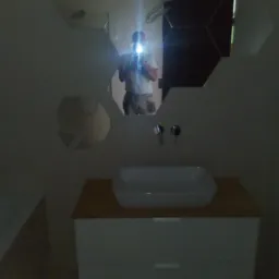 Nowoczesna łazienka z umywalką nablatową na szafce z szufladami, lustro w kształcie plastra miodu odbija osobę robiącą zdjęcie telefonem.