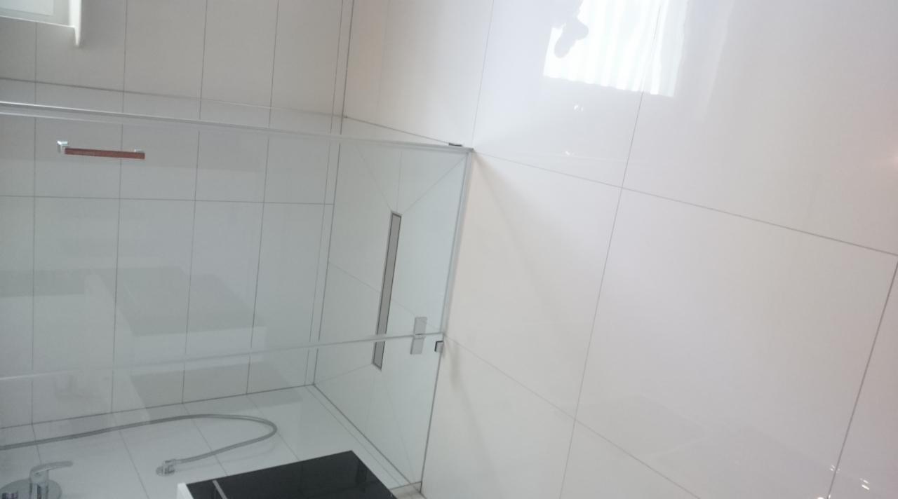 Biała łazienka z kabiną prysznicową typu walk-in, wykończona błyszczącymi, kwadratowymi płytkami ceramicznymi, widoczne chromowane elementy armatury i odpływ liniowy w podłodze.