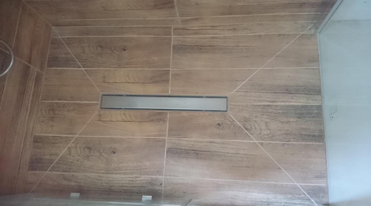 Ułożona podłoga z drewnopodobnych płytek w kabinie prysznicowej ze stalowym odpływem liniowym, wykonana w Skarżysku-Kamiennej.