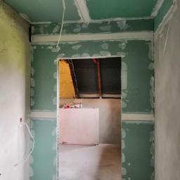 Kryształ - Wnętrze w trakcie prac wykończeniowych, widoczne zielone płyty na ścianach i suficie, łączenia wzmocnione taśmą, surowy stan, widok na pomieszczenie obok z izolacją i elementami konstrukcyjnymi dachu.