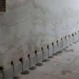 Rząd nawierconych otworów wzdłuż ściany przy podłodze, przygotowanych do iniekcji preparatu osuszającego, widoczna wilgoć na ścianie i podłodze.