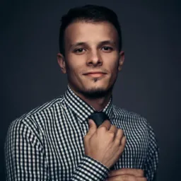 Portret młodego mężczyzny w koszuli w kratę, poprawiającego krawat na ciemnym tle. Stonowana kolorystyka, profesjonalne oświetlenie.