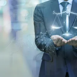 Mężczyzna w garniturze prezentuje na dłoniach cyfrową wizualizację wagi sprawiedliwości, z nałożonym w tle zarysem budynku.