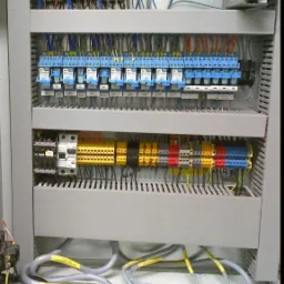 Wnętrze szafy sterowniczej z widocznymi stycznikami, bezpiecznikami i listwami zaciskowymi, okablowanie uporządkowane z wykorzystaniem oznaczników.