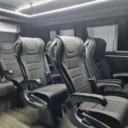 Wnętrze luksusowego busa z czarnymi, skórzanymi fotelami pasażerskimi, przeszywanymi ścianami i zasłonami w oknach.