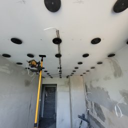 RoKa Renovation Robert Karpiński - Wnętrze w trakcie remontu: sufit z zamontowanymi punktami oświetleniowymi, ściany w szpachli, poziomica laserowa. Widoczne przewody elektryczne.