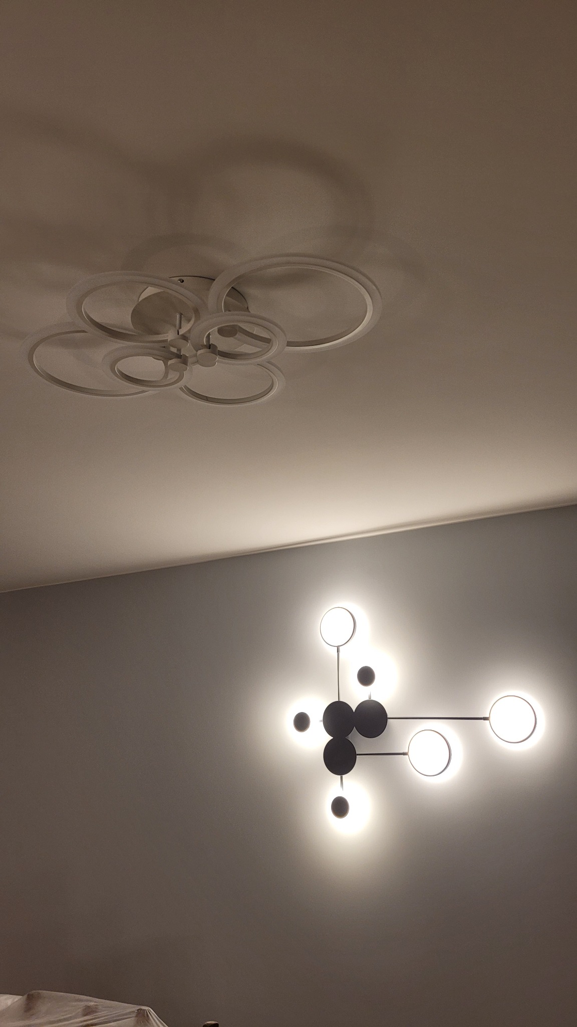 Nowoczesne oświetlenie: okrągła lampa sufitowa LED i designerski kinkiet z kulistymi punktami świetlnymi na szarej ścianie. Minimalistyczny wystrój wnętrza.