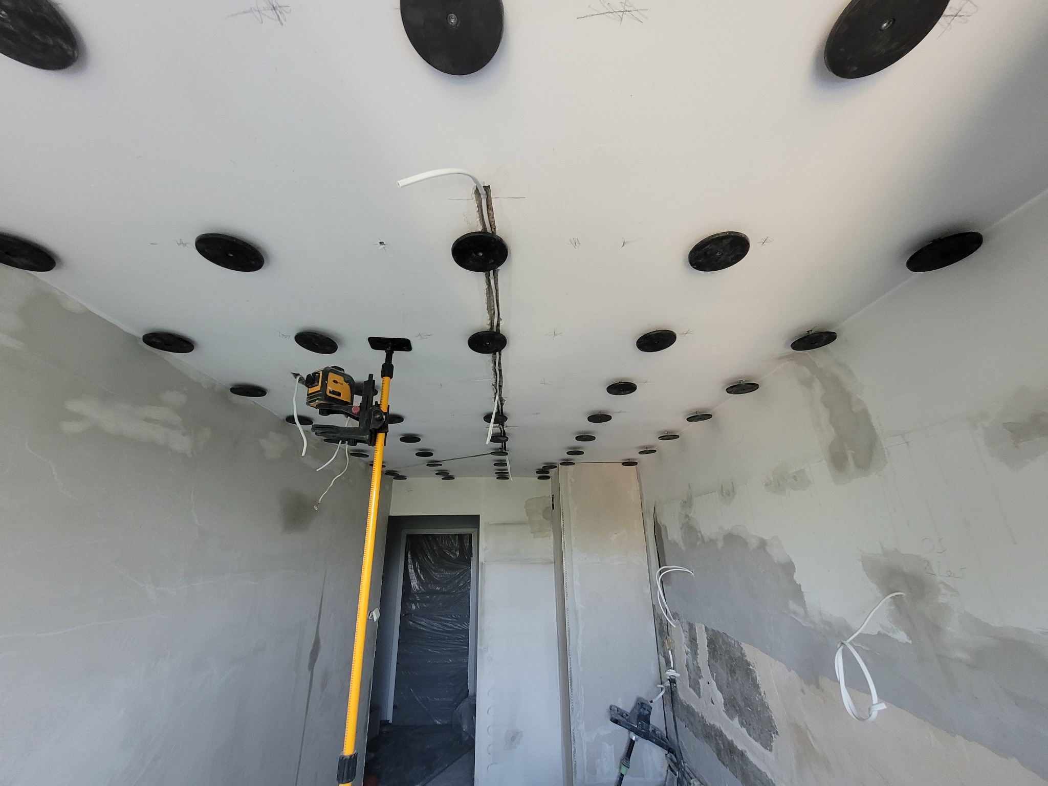 Wnętrze w trakcie remontu: sufit z zamontowanymi punktami oświetleniowymi, ściany w szpachli, poziomica laserowa. Widoczne przewody elektryczne.