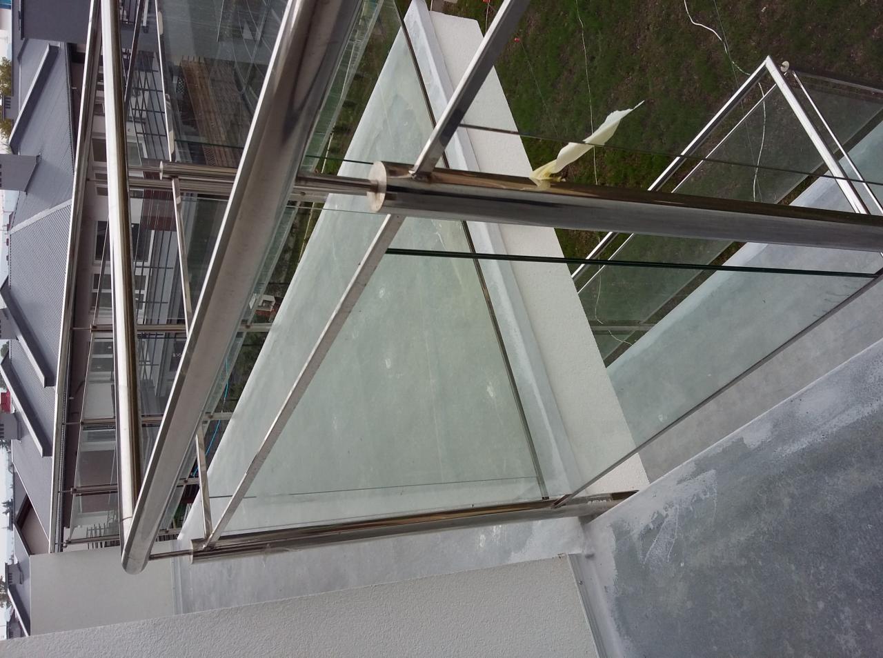 Szklana balustrada z elementami ze stali nierdzewnej na balkonie, widok z góry, w tle zabudowa miejska.