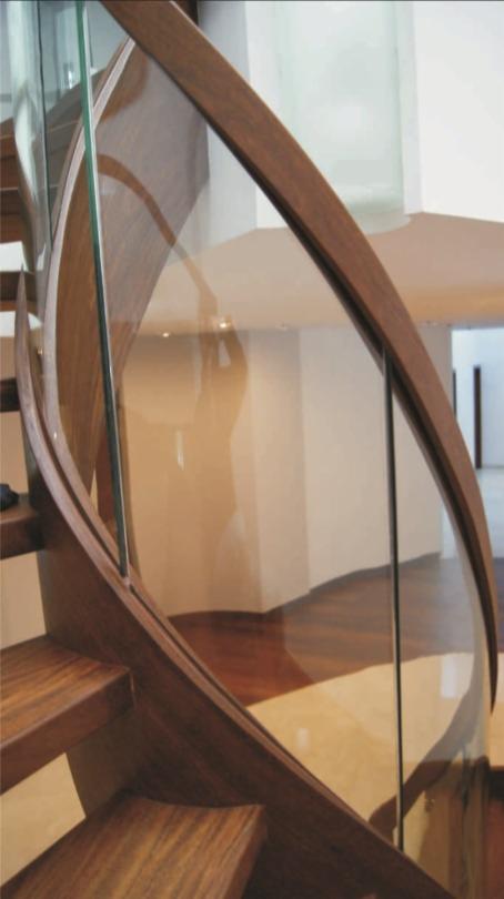 Zakrzywiona drewniana konstrukcja schodów z przezroczystą szklaną taflą, tworząca nowoczesną barierkę.