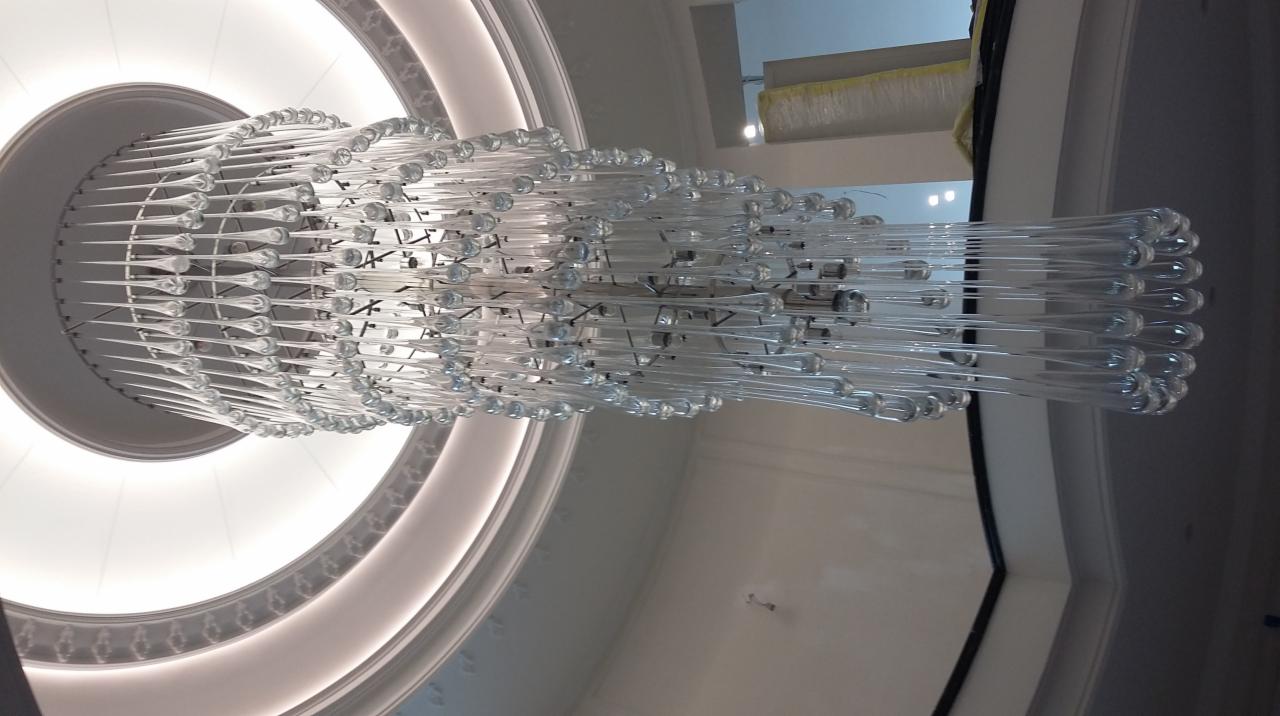 Wielopoziomowy żyrandol z przezroczystych, szklanych elementów w kształcie sopli, zamontowany na suficie z dekoracyjnym oświetleniem obwodowym.