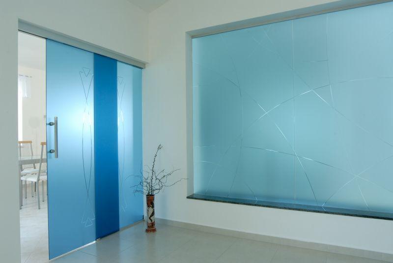 Szklane drzwi przesuwne w odcieniach błękitu z geometrycznym wzorem i szklana ściana z abstrakcyjnym motywem, w nowoczesnym wnętrzu z ceramiczną podłogą.