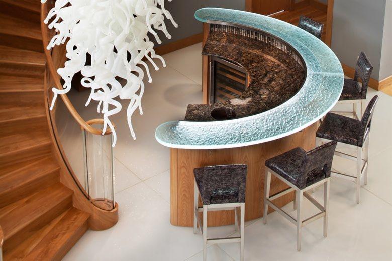 Wnętrze z drewnianymi schodami z przeszkloną balustradą, barem z blatem z granitu i szkła oraz szklaną lampą wiszącą.