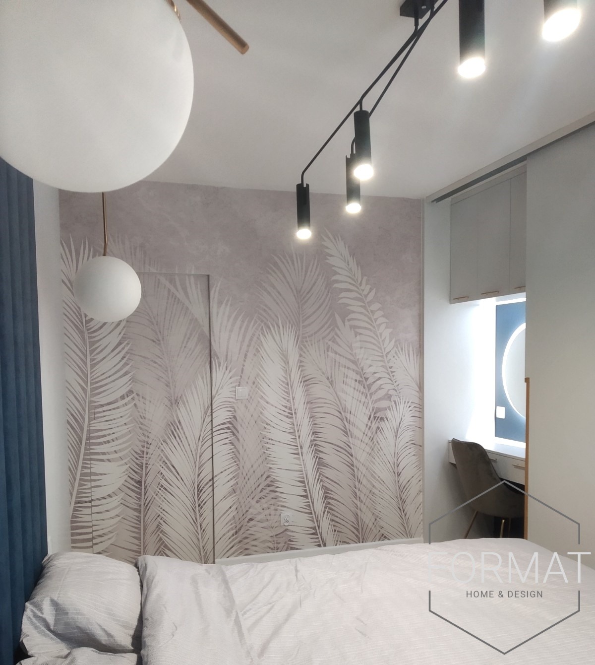 Sypialnia z tapetą w motywy tropikalne, oświetleniem punktowym i wiszącymi lampami kulistymi, biurko z okrągłym lustrem w tle. Na ścianie widoczne ukryte drzwi.