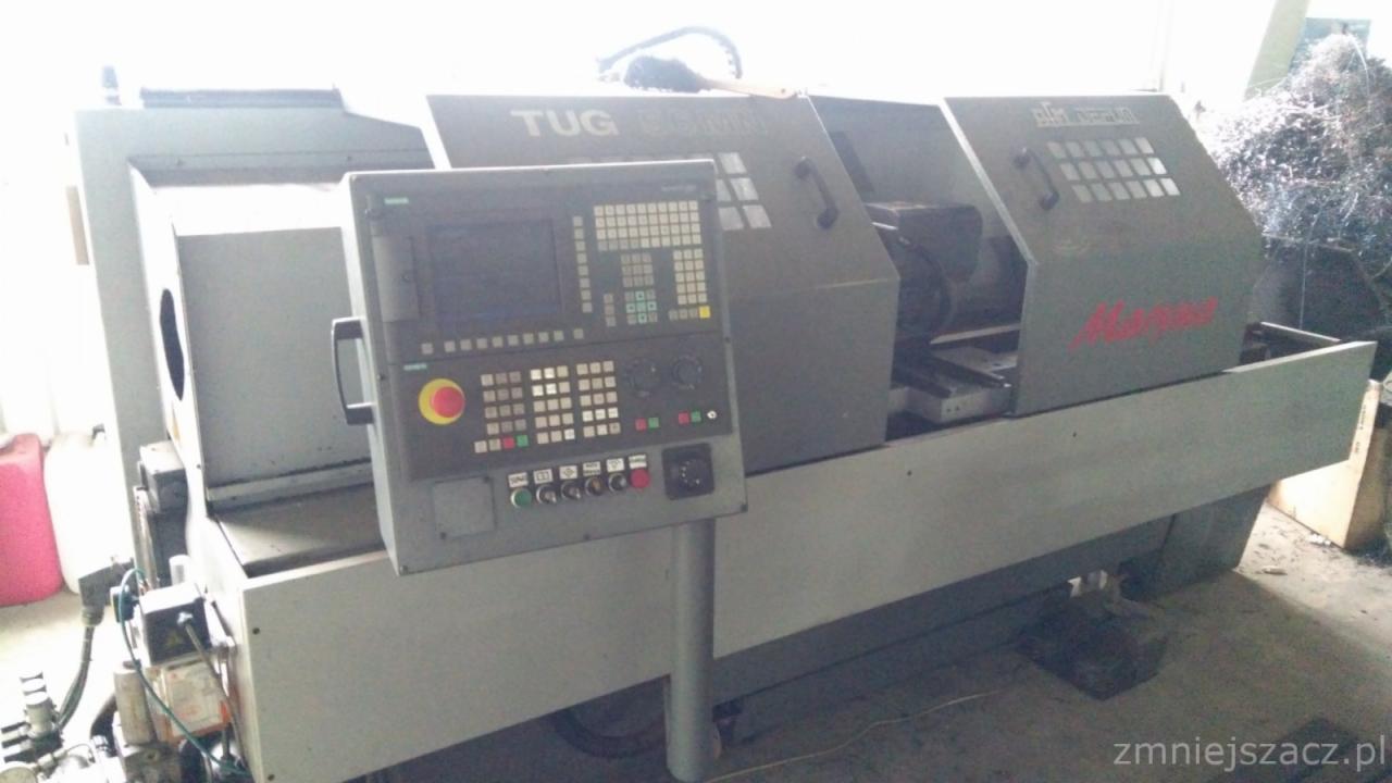 Szara tokarka CNC TUG z panelem sterowania i stertą wiórów metalowych w tle.