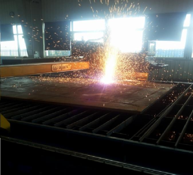 Automatyczne cięcie plazmowe grubej, ciemnej blachy stalowej na ruszcie, iskry i jasne światło w hali produkcyjnej z oknami.