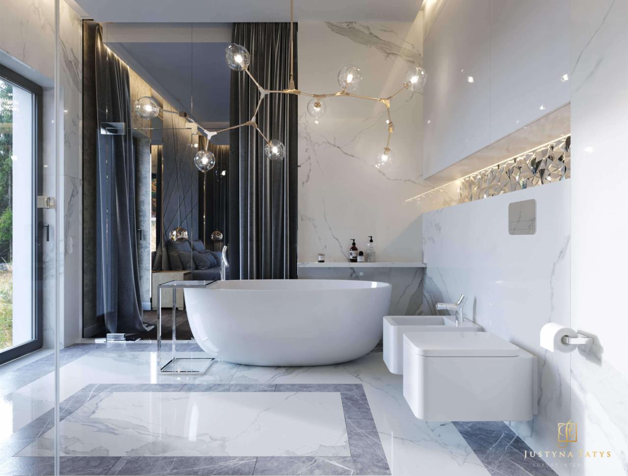 Elegancka łazienka z wolnostojącą wanną i marmurowymi płytami, oświetlona nowoczesnym, rozgałęzionym żyrandolem, z widokiem na sypialnię przez szklaną ścianę.