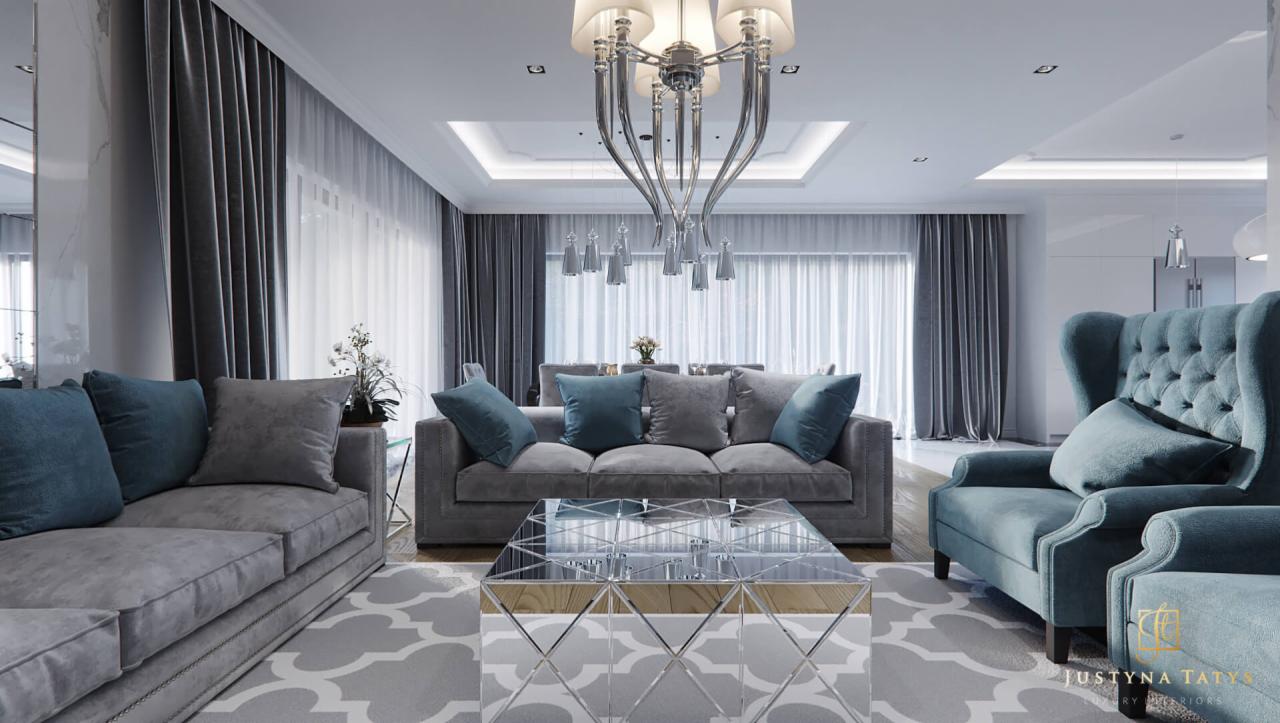 Elegancki salon z szarymi sofami, turkusowymi poduszkami i fotelami, lustrzanym stolikiem kawowym oraz nowoczesnym żyrandolem, oświetlony naturalnym światłem wpadającym przez okna z długimi...