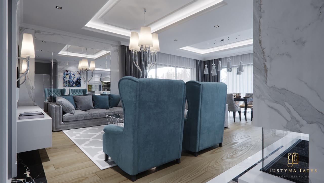 Elegancki salon z turkusowymi fotelami typu uszak, szarą sofą i marmurowymi akcentami, oświetlony wiszącymi lampami i z dekoracyjnym lustrem na ścianie.
