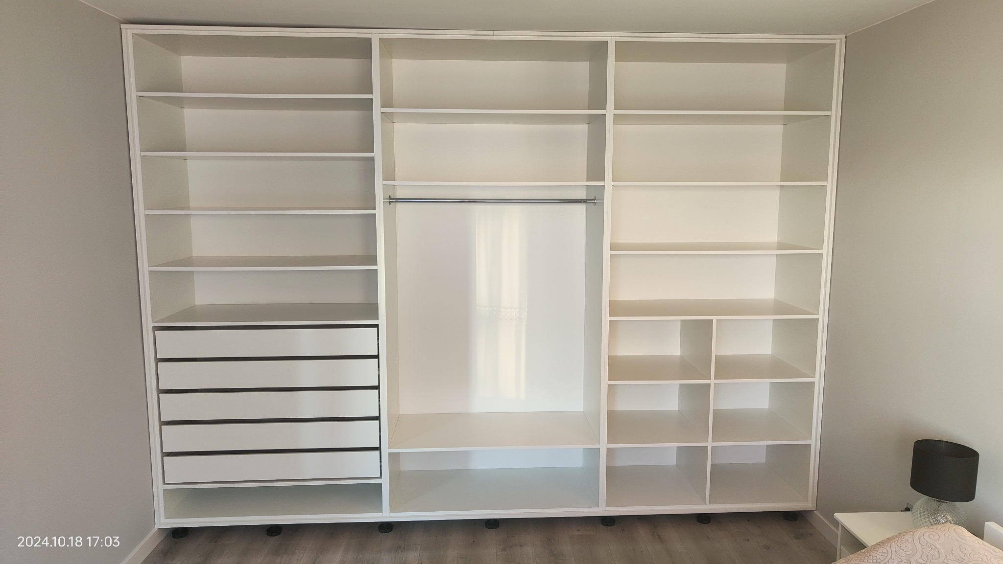 Biała szafa wnękowa z szufladami i półkami, widok z przodu, minimalistyczny design, oświetlenie dzienne, widoczne detale wykończenia, brak elementów dekoracyjnych.