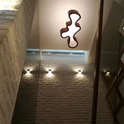 Nowoczesne wnętrze klatki schodowej z ceglaną ścianą, designerską lampą wiszącą i drewnianymi elementami dekoracyjnymi.