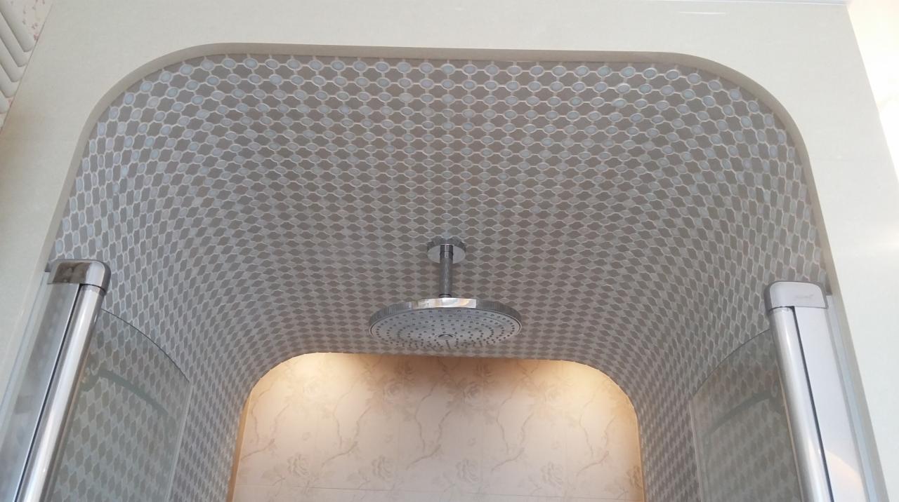 Kopuła prysznicowa wyłożona mozaiką w odcieniach szarości i bieli, z okrągłą deszczownicą zamontowaną centralnie, widok od dołu.