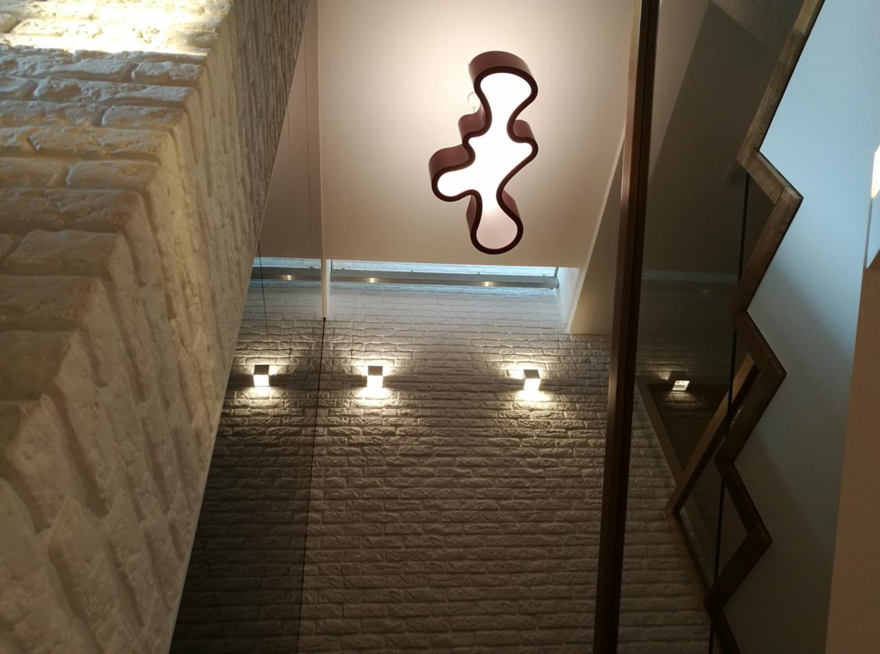 Nowoczesne wnętrze klatki schodowej z ceglaną ścianą, designerską lampą wiszącą i drewnianymi elementami dekoracyjnymi.
