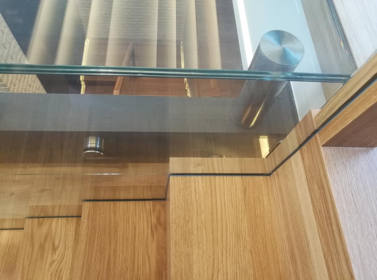 Szczegółowe ujęcie drewnianych schodów z szklaną balustradą i metalowymi wspornikami, widok z góry.