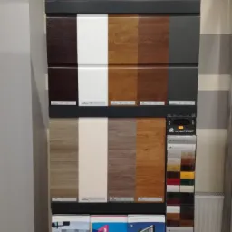 Ekspozycja próbek kolorów i faktur paneli marki Wiśniowski i Aliprof, prezentująca różne odcienie drewna, szarości i bieli, wraz z katalogami bram.