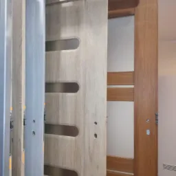 Ekspozycja kilku modeli drzwi wewnętrznych z przeszkleniami, prezentowanych w salonie sprzedaży. Drzwi w odcieniach drewna, z różnymi wykończeniami i okuciami.