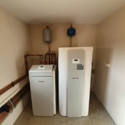 Dwa białe urządzenia Stiebel Eltron z widocznymi miedzianymi rurami i zbiornikami wyrównawczymi w jasnym pomieszczeniu.