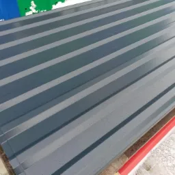 Stos arkuszy blachy trapezowej w kolorze grafitowym, ułożonych na drewnianych legarach z widocznymi kroplami wody na powierzchni.