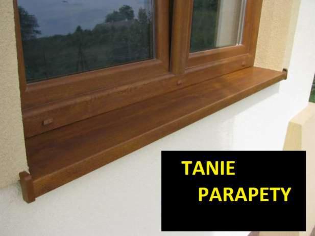 Okno z drewnianą ramą i parapetem zewnętrznym w kolorze orzecha, zamontowane w elewacji budynku. Widoczny fragment okna z widokiem na zieleń za oknem.