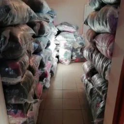 Magazyn z rzędami worków foliowych wypełnionych odzieżą, widok korytarza między stertami.