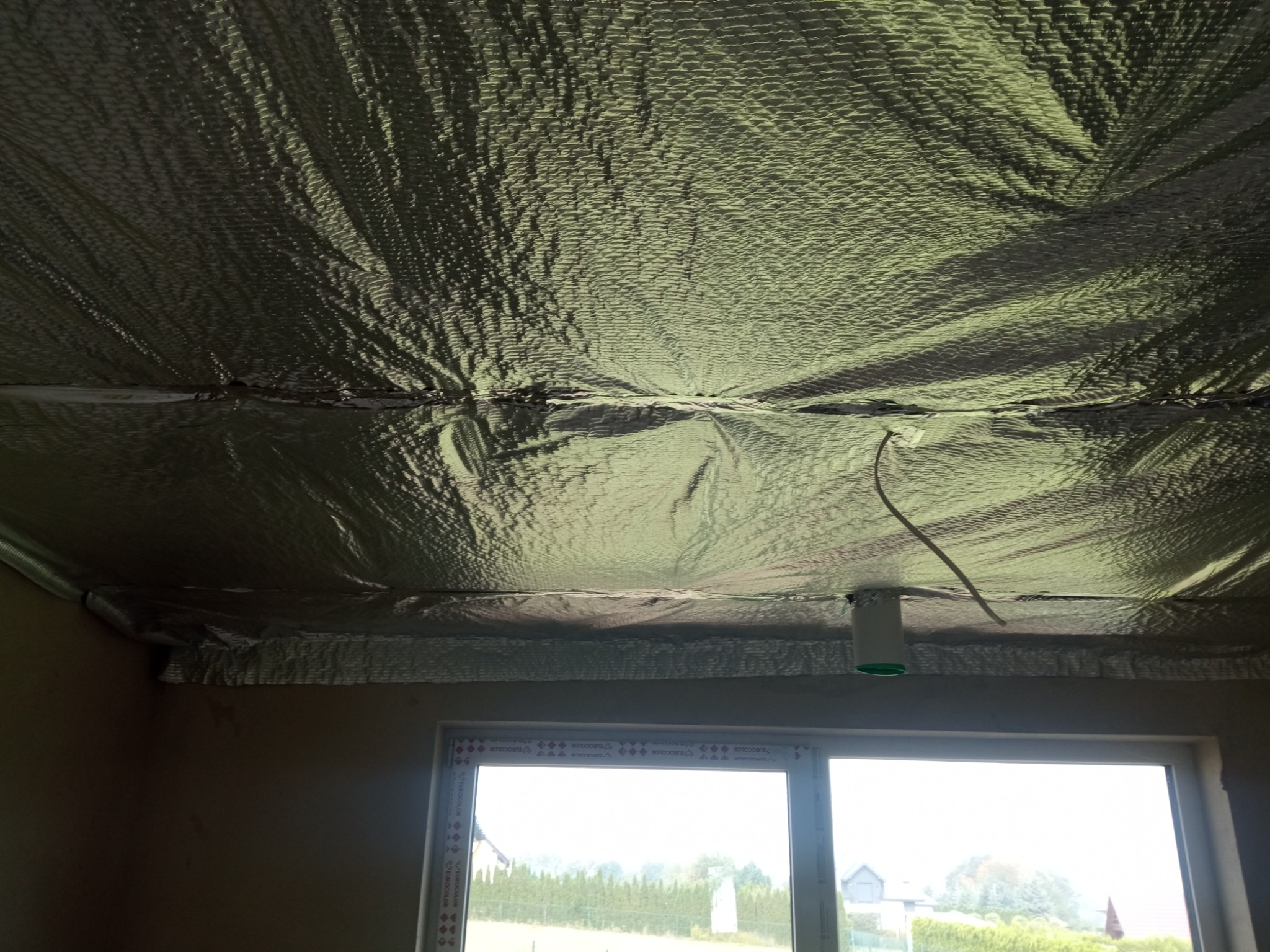 Folia termoizolacyjna na poddaszu w domu w Bystrej, widok z dołu na zabezpieczoną przestrzeń nad oknem.