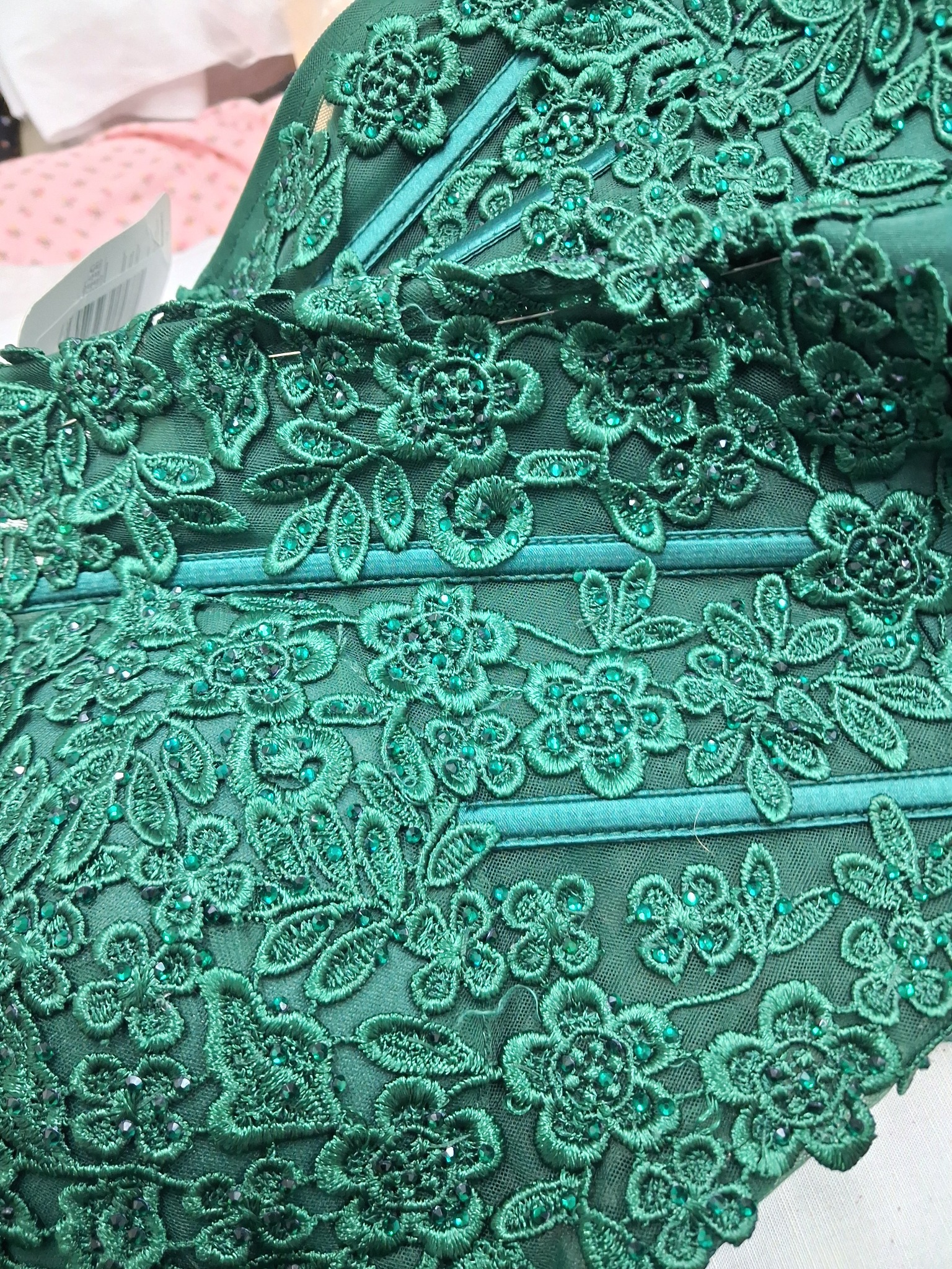 Fragment zielonej, zdobionej koronki z kwiatowym wzorem i błyszczącymi koralikami, ukazujący precyzję wykonania i dbałość o detale w szyciu odzieży.
